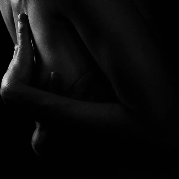 Polyamorie en intimiteit 1 Zwart-witfoto van een arm op een blote torso, rustend op de huid tegen een zwarte achtergrond.